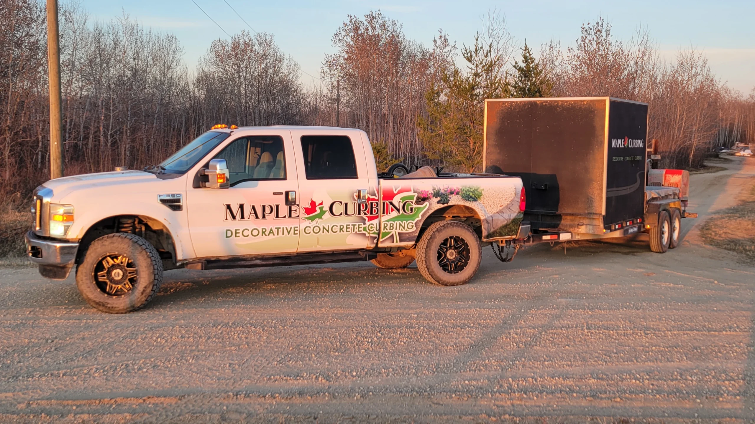 MapleCurbing truck and trailer parked on a gravel road at sunset
